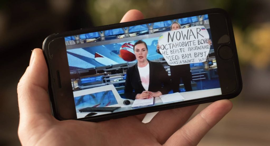 Viewing on a phone the sequence when a Russian journalist brandishes an anti-war placard during the Russian news. Photo credit: Romain Longieras / Hans Lucas via Reuters Connect