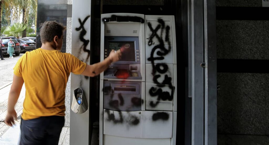 A protestor sprays an ATM machine of a local bank in Beirut, August 2024. Photo credit: Marwan Naamani/dpa via Reuters Connect.